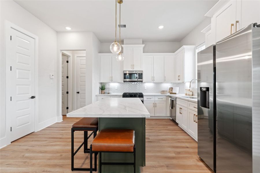 The kitchen is centered around a statement island with contrasting cabinetry, creating both a functional workspace and a natural gathering point within the home.