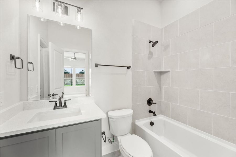 Bathroom with gray vanity, white countertop, tub-shower combo with tile surround, and dark fixtures Bathroom with gray vanity, white countertop, tub-shower combo with tile surround, and dark fixtures