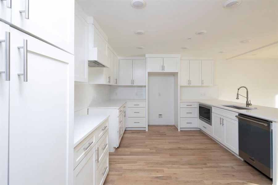 Kitchen featuring stainless steel appliances, a sink, white cabinetry, light countertops, and light wood finished floors