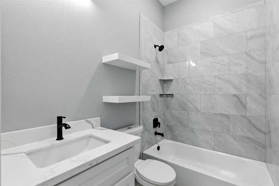 This bathroom features a modern design with a sleek white vanity, black fixtures, and a spacious bathtub. The walls and shower area are adorned with elegant gray tiles, creating a clean and sophisticated look.