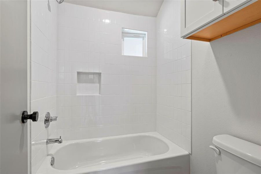 Bathroom featuring tiled shower / bath combo and toilet