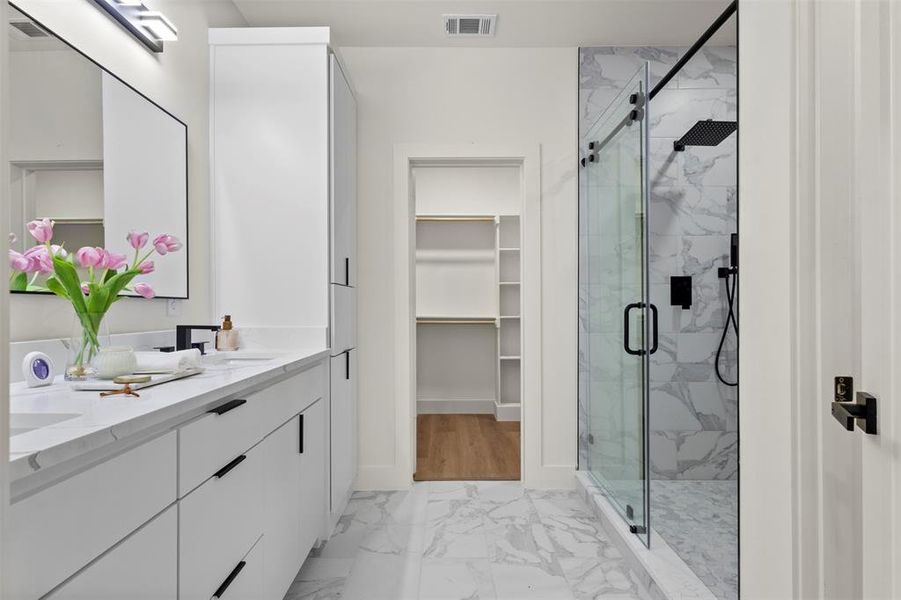 Full bath featuring double vanity, light marble finish floors, a marble finish shower, and a spacious closet