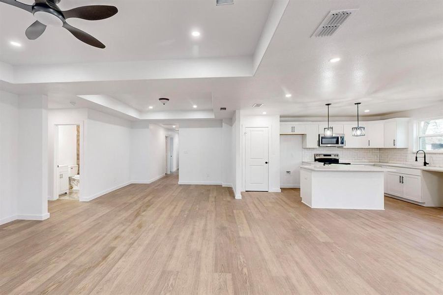 Unfurnished living room featuring a tray ceiling, light hardwood / wood-style flooring, ceiling fan, and sink