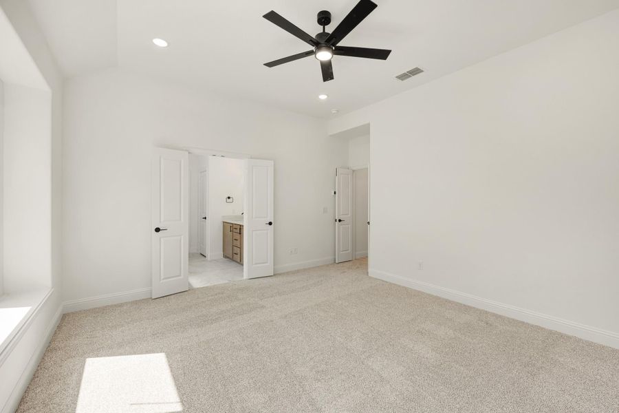 Empty bedroom with carpet, black ceiling fan, and open door to ensuite bathroom