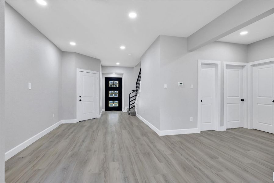 This modern entryway features sleek wood flooring, neutral walls, and recessed lighting. It includes multiple doors leading to other rooms and a staircase with a contemporary railing, enhancing the open and inviting space.