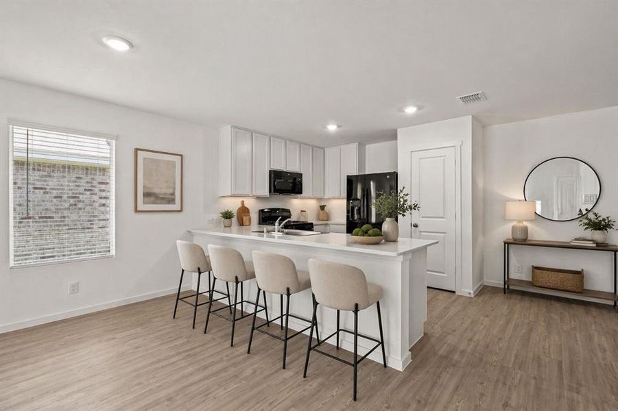 Open-concept kitchen and living area featuring wood-finish flooring, white cabinetry, integrated black appliances, recessed lighting, and a kitchen island with seating