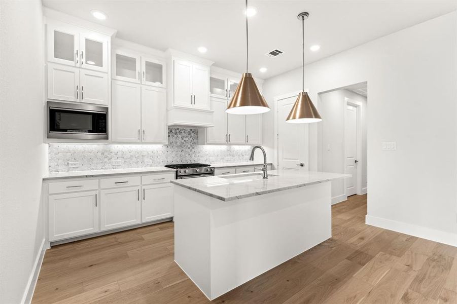 Kitchen featuring built in microwave, sink, white cabinetry, hanging light fixtures, and a kitchen island with sink