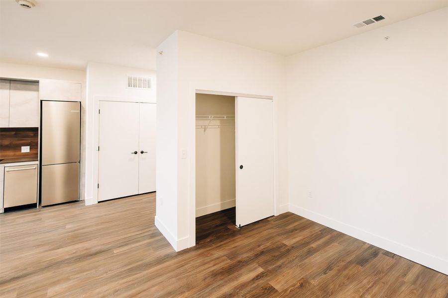 Unfurnished bedroom with stainless steel refrigerator, light wood-style floors, and a closet