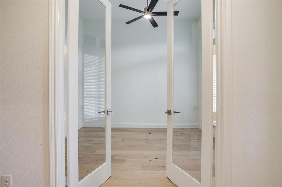 Large study featuring French doors with inlaid glass, ceiling fan and large window for natural lighting.