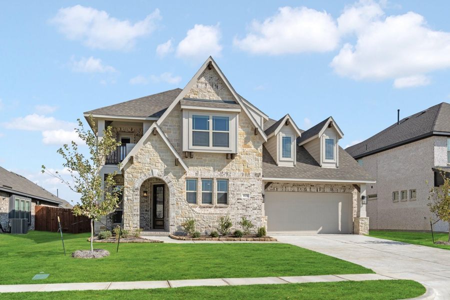 Two-story stone and brick home with arched entry, two-car garage, and manicured front lawn