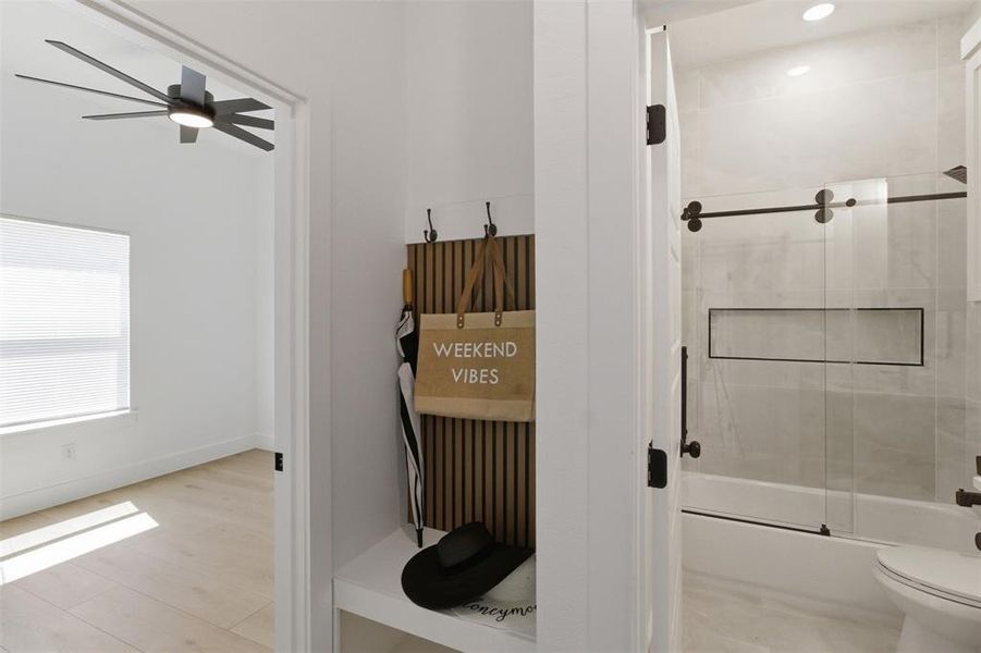 Bathroom featuring a bathtub with a sliding glass door and matte black hardware, recessed wall niche, and light-toned tile surround
