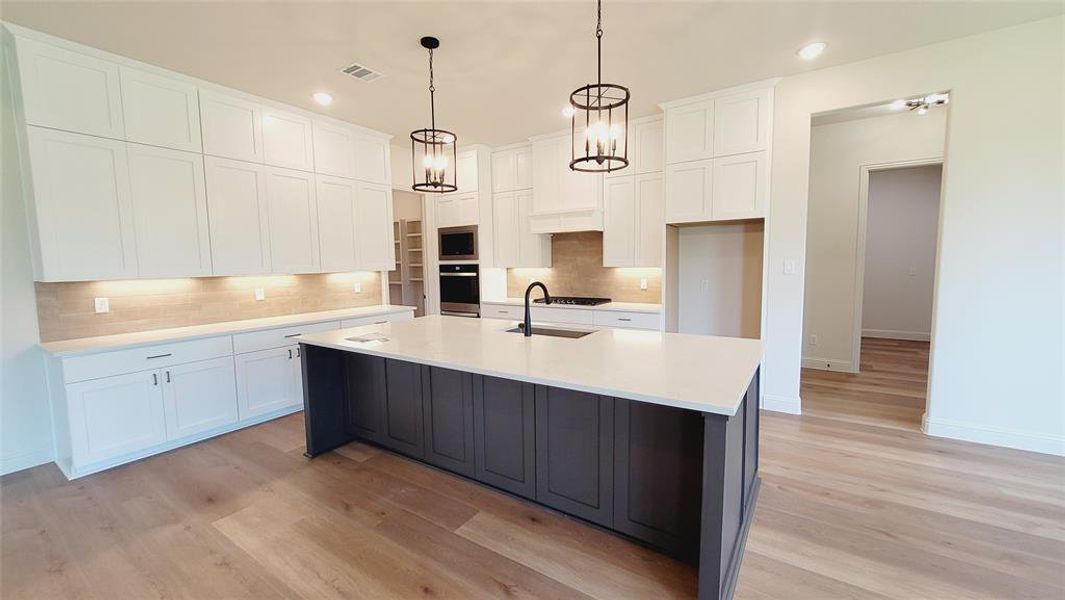 Modern kitchen featuring an expansive center island with seating, white shaker cabinetry, stainless steel appliances, and wood-finish flooring