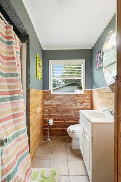 Full bath featuring vanity, ornamental molding, a wainscoted wall, light tile patterned floors, and a shower with shower curtain Full bath featuring vanity, ornamental molding, a wainscoted wall, light tile patterned floors, and a shower with shower curtain