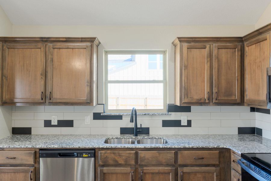 Kitchen with stainless steel dishwasher, light stone counters, tasteful backsplash, and wood finish cabinets