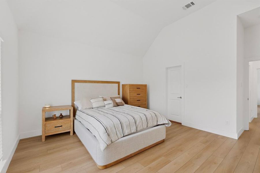 Bright bedroom featuring vaulted ceilings, light wood-finish flooring, white baseboards, and a white door with contemporary hardware Bright bedroom featuring vaulted ceilings, light wood-finish flooring, white baseboards, and a white door with contemporary hardware