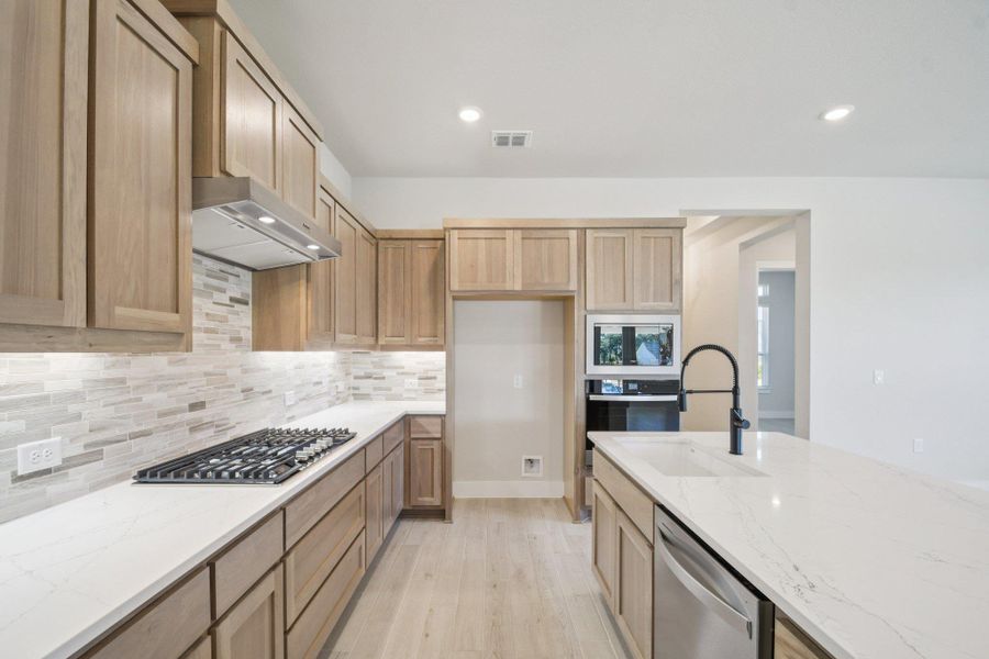 Kitchen featuring light stone counters, light wood-style flooring, decorative backsplash, recessed lighting, and appliances with stainless steel finishes