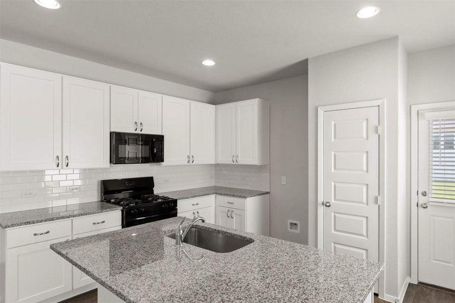 Kitchen with black appliances, an island with sink, dark wood-style flooring, tasteful backsplash, and light stone countertops