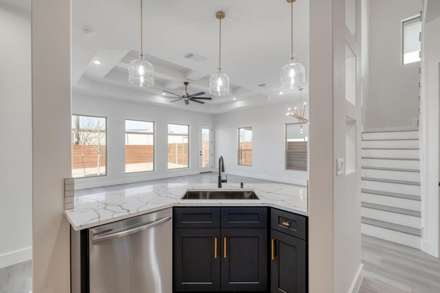 Kitchen with light stone countertops, visible vents, a sink, pendant lighting, and dishwasher