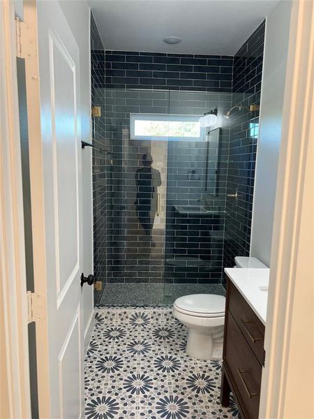 Bathroom with toilet, vanity, tile patterned floors, and a tile shower