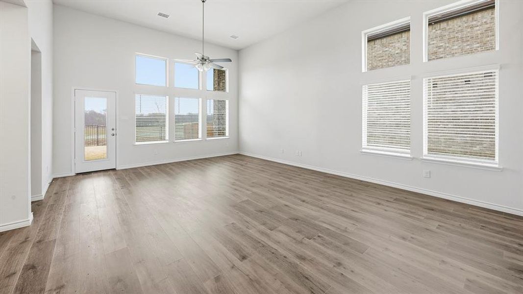 Spacious living area featuring high vaulted ceilings, light wood-finish flooring, a contemporary ceiling fan, and multiple large windows with white blinds