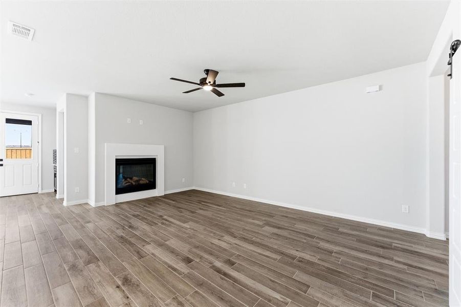 Unfurnished living room featuring a barn door, wood finished floors, a glass covered fireplace, and a ceiling fan