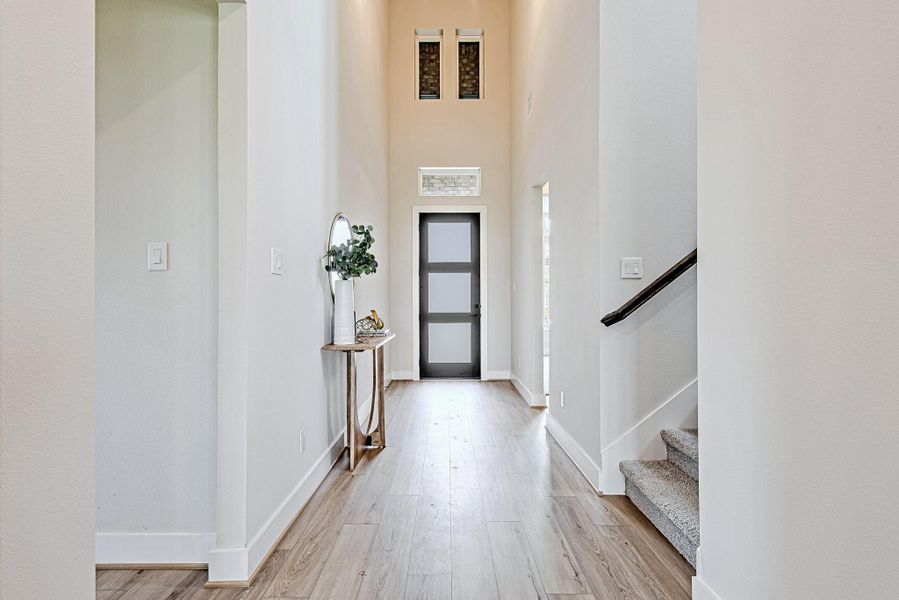 A dramatic foyer welcomes you with sky-high ceilings, transom windows, and natural light that pours in through the frosted glass front door—with the staircase to the second floor thoughtfully positioned just to the right.