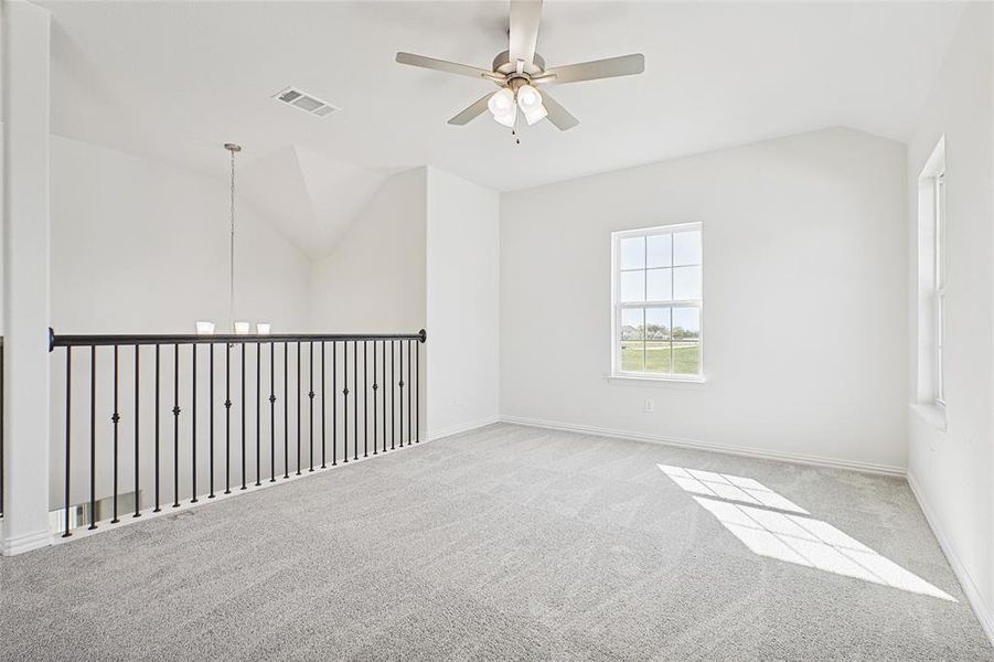 Carpeted empty room featuring vaulted ceiling and ceiling fan with notable chandelier