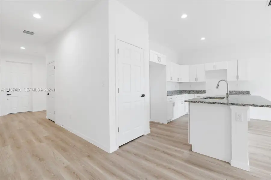 Kitchen featuring white cabinetry, stone-finish countertops, an integrated island, a stainless steel faucet, and wood-finish flooring Kitchen featuring white cabinetry, stone-finish countertops, an integrated island, a stainless steel faucet, and wood-finish flooring