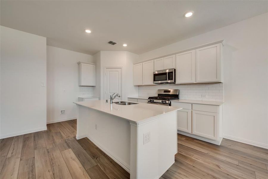 Kitchen with white cabinetry, light wood-type flooring, a center island with sink, appliances with stainless steel finishes, and sink