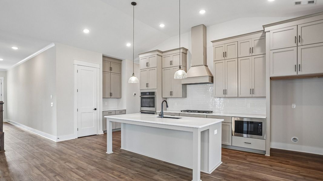 Kitchen with ceiling-height cabinetry, quartz countertops, walk-in pantry, built-in ovens, and gas range