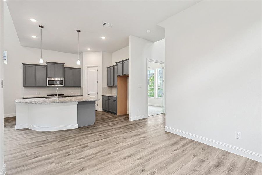 Kitchen with light hardwood / wood-style floors, a kitchen island with sink, light stone countertops, and gray cabinets