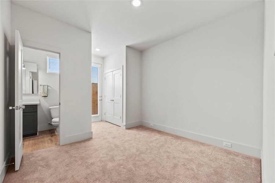 This bright, carpeted room features neutral walls, access to the Jack and Jill bathroom with modern fixtures, and a door leading outside, filling the space with natural light and adding extra convenience.