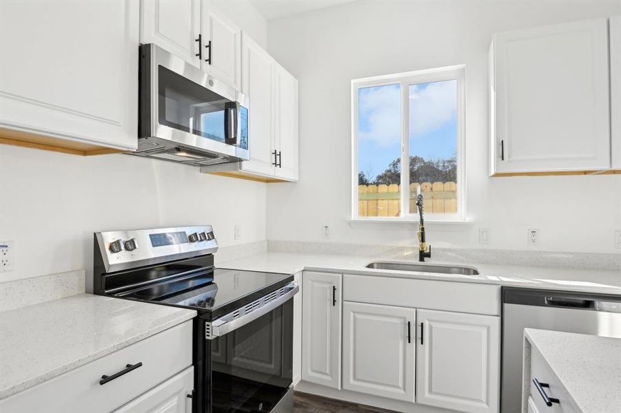 Kitchen with appliances with stainless steel finishes, a sink, white cabinetry, and light stone countertops