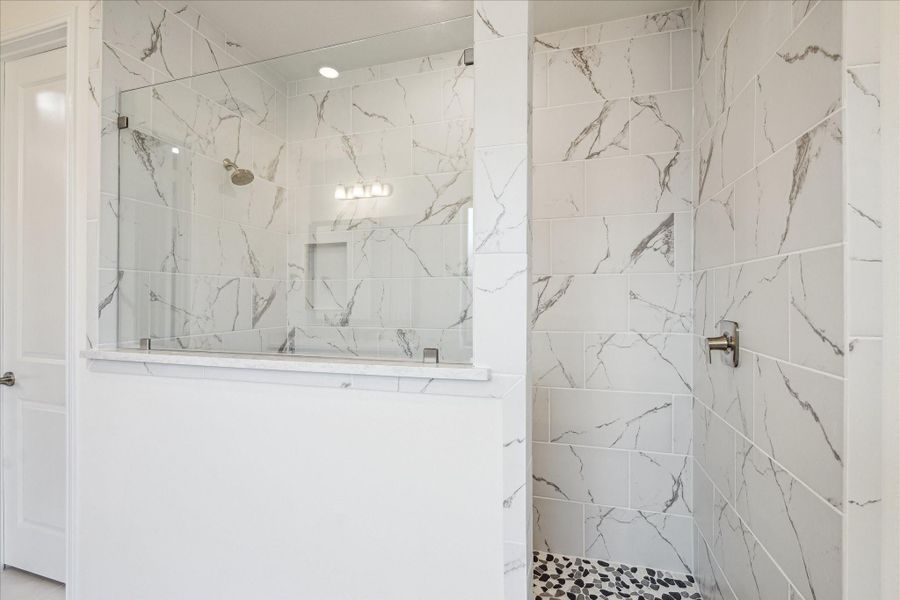 An upgraded, spacious shower is the centerpiece, highlighted by elegant marble-style tile extending from floor to ceiling. A unique flooring design and a recessed shower shelf add both function and elevated style.