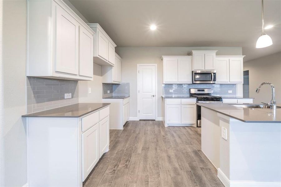 Kitchen featuring grey backsplash, white cabinets and grey quartz countertops.  Door goes into walk in pantry