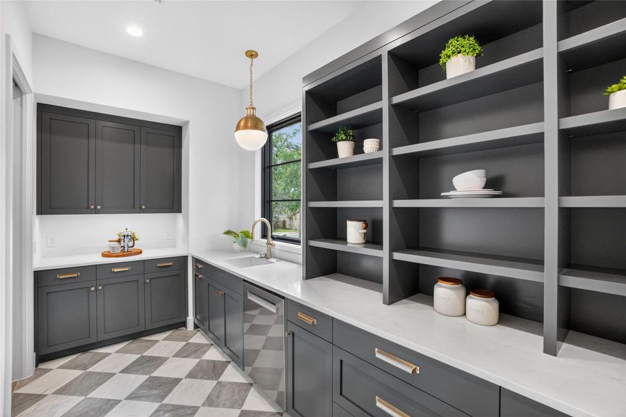 A well-appointed scullery features ample built-in shelving, elegant cabinetry, and a checkerboard floor design.