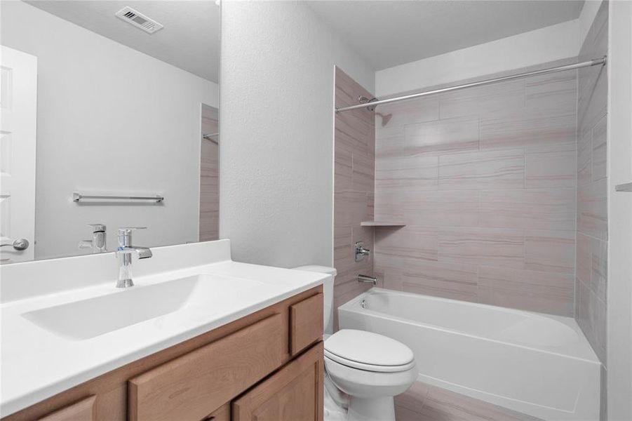 Secondary bath features tile flooring, bath/shower combo with tile surround, white stained wood cabinets, beautiful light countertops, mirror, dark, sleek fixtures and modern finishes.