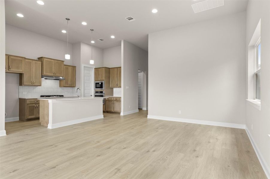Kitchen with brown cabinets, under cabinet range hood, light wood-type flooring, backsplash, and built in microwave
