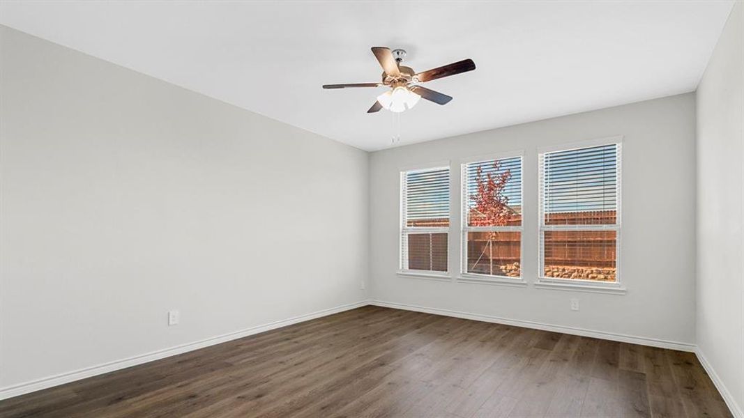 Spacious room featuring wood-finish flooring, three large windows with horizontal blinds, a ceiling fan with integrated lighting, and neutral wall paint