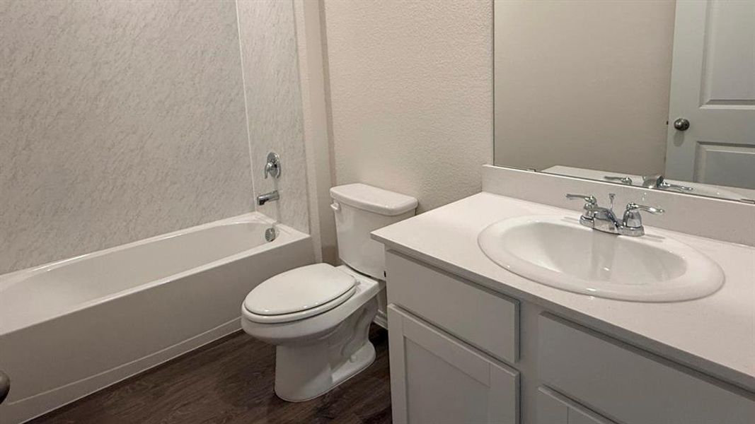 Bathroom featuring a textured wall, vanity, bathing tub / shower combination, and dark wood-style flooring Bathroom featuring a textured wall, vanity, bathing tub / shower combination, and dark wood-style flooring