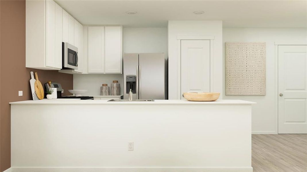 Kitchen with stainless steel appliances, light countertops, light wood-style floors, white cabinetry, and a peninsula