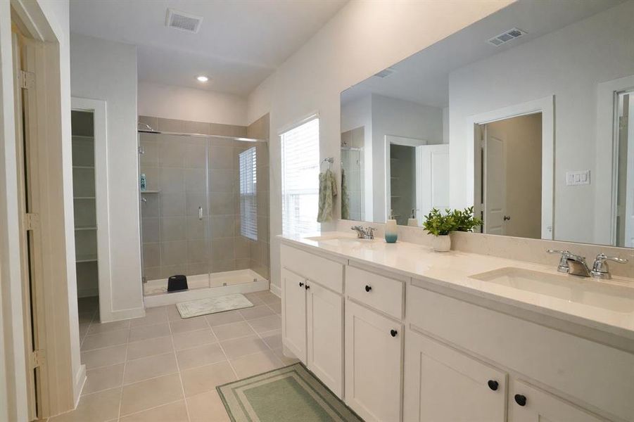 Bathroom featuring a dual vanity with undermount sinks and chrome fixtures, a spacious walk-in shower with tile surround and glass enclosure, and neutral tile flooring