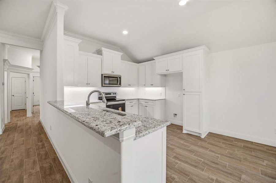 The kitchen features white cabinetry, granite countertops, and stainless steel appliances, including a microwave and range