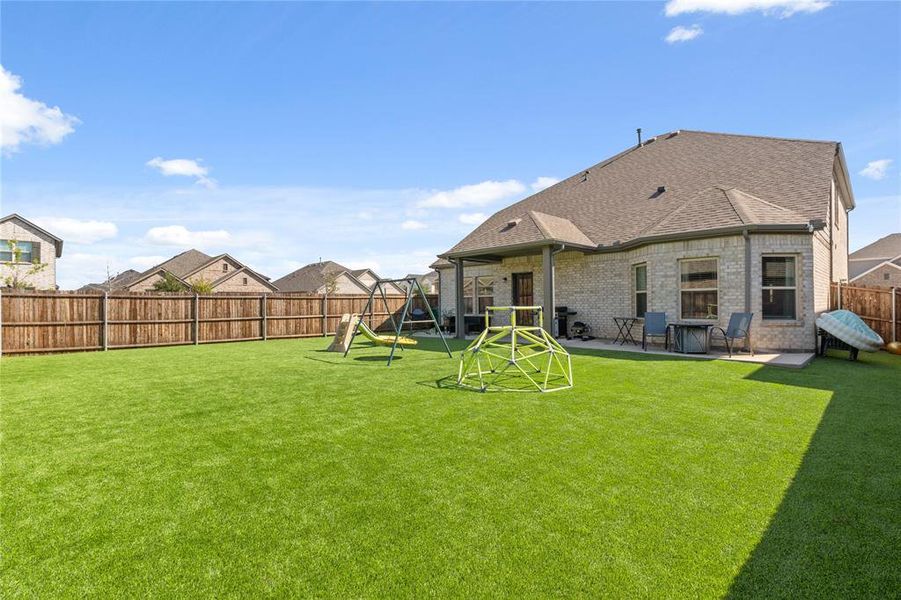 Rear view of house with a spacious fenced backyard, a shingled roof, a patio area, a playground, and brick siding