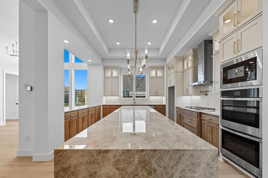 Kitchen with a chandelier, light stone countertops, glass insert cabinets, brown cabinets, and recessed lighting Kitchen with a chandelier, light stone countertops, glass insert cabinets, brown cabinets, and recessed lighting