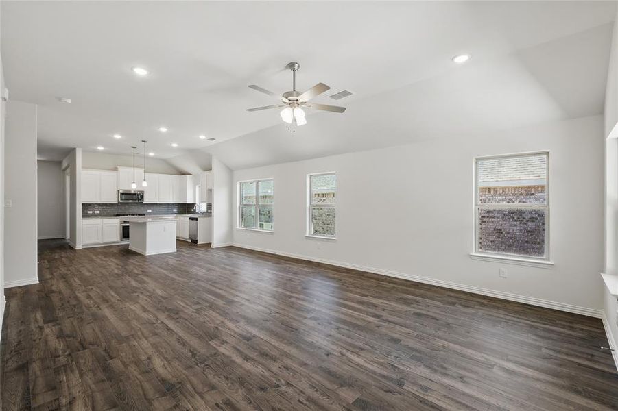 Unfurnished living room with dark wood finished floors, lofted ceiling, visible vents, ceiling fan, and baseboards