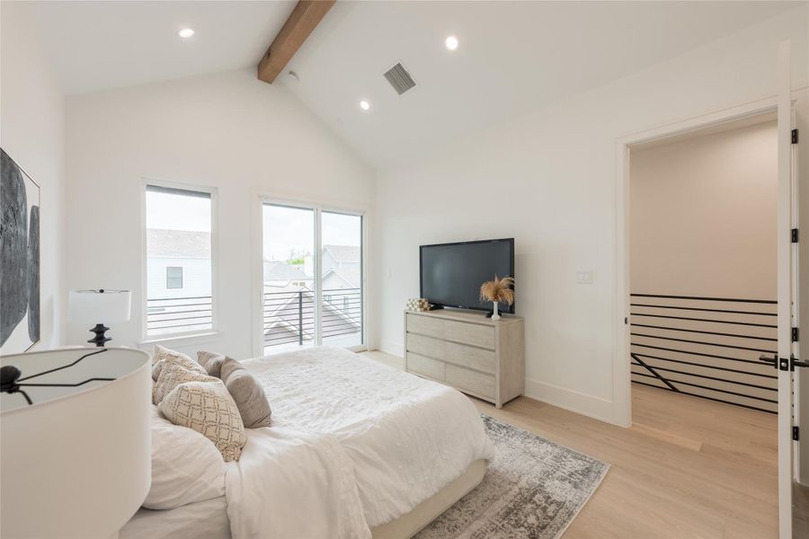Architectural notes from the primary bedroom: vaulted ceiling with natural wood tie beam, recessed can lighting, sliding glass balcony access paired with a vertical sidelight, open pass-through to the stair landing, horizontal black metal railing detail, and wide-plank white oak flooring.