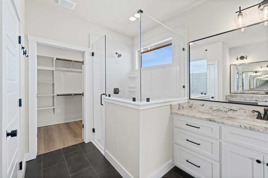 Full bath featuring dark tile patterned floors, vanity, a stall shower, and a spacious closet