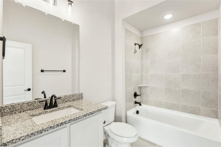 Bathroom with granite countertop vanity, white cabinets, and tiled tub-shower combo with black fixtures