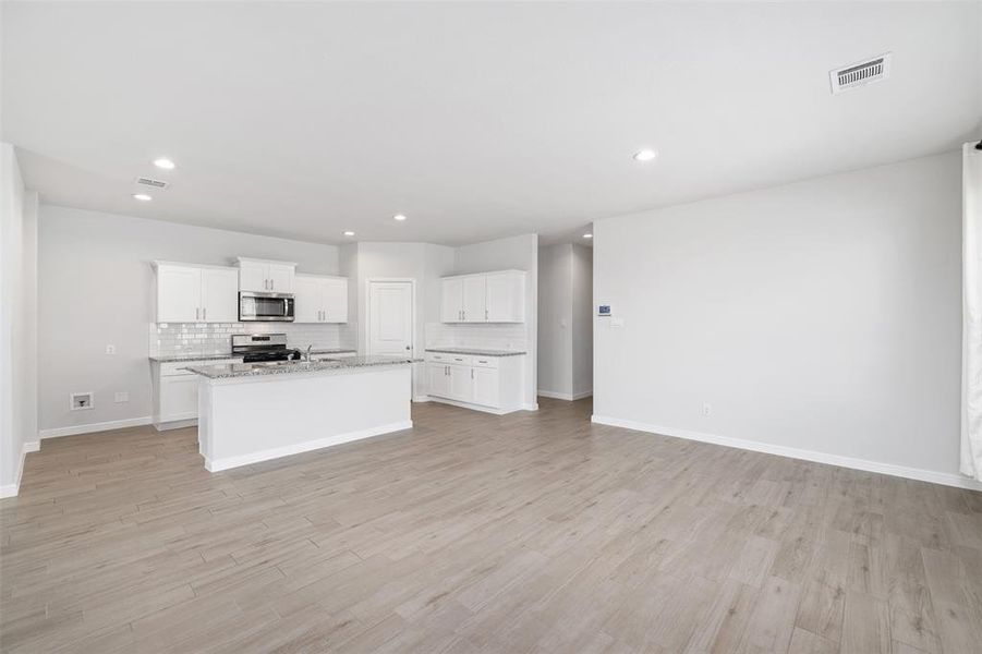 Kitchen featuring light stone counters, light hardwood / wood-style flooring, a center island with sink, stainless steel appliances, and white cabinets